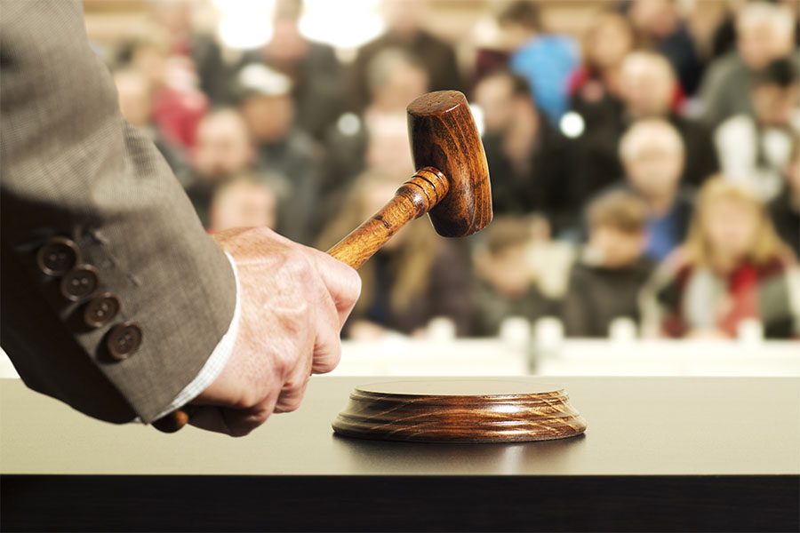 Auctioneer Bonds - Closeup View of an Auctioneer Holding a Gavel with Views of Many Blurred People Sitting in the Background