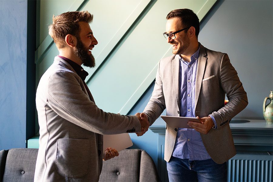 Bonds - Portrait of Two Cheerful Young Businessmen Standing in the Office Shaking Hands