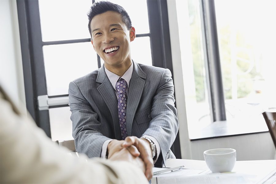 Client Center - Closeup Portrait of a Smiling Young Businessman Sitting in a Modern Office While Shaking Hands with a Business Colleague