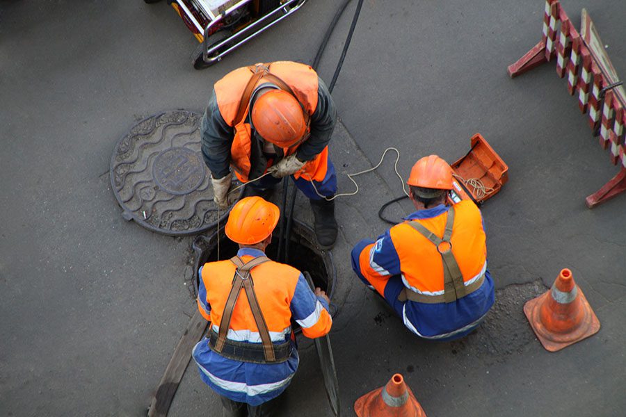 License and Permit Bonds - Portrait of Three Construction Workers Inspecting the Sewer System in a City