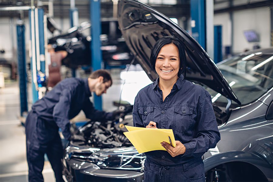 Miscellaneous PA Motor Vehicle Business Bonds - View of a Female Mechanic Holding Paperwork and Standing in Front of a Car in a Garage Repair Shop