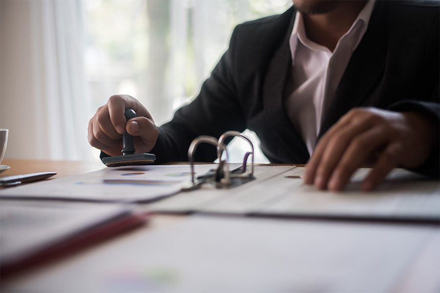 Public Official Bonds - Closeup View of a Man Wearing a Suit Sitting in the Office While Stamping Papers in a Binder