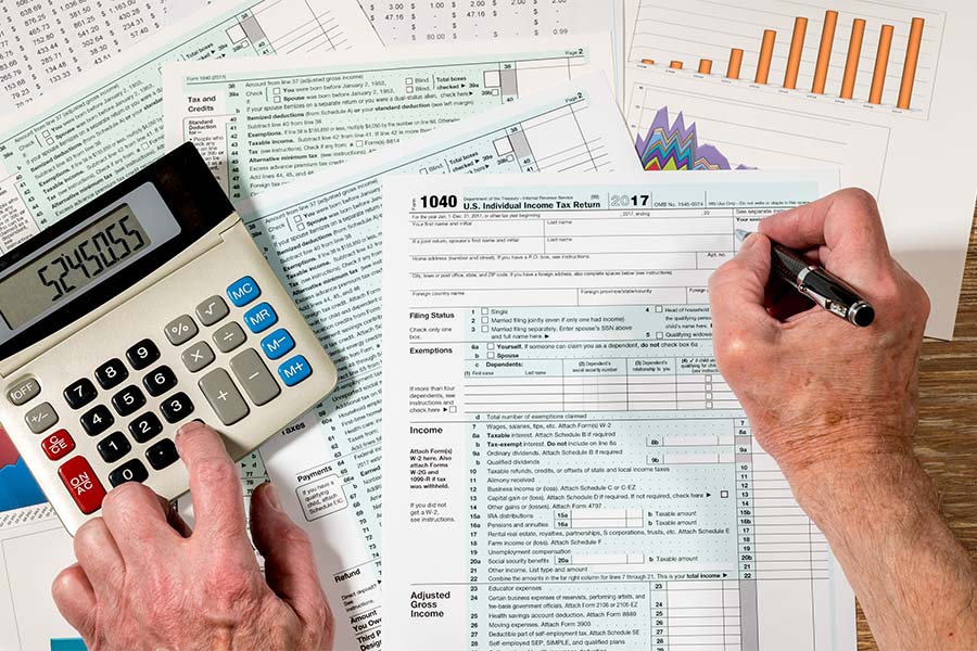 Tax Preparer Insurance - Closeup View of a Tax Preparers Hands Working on Tax Documents and Using a Calculator